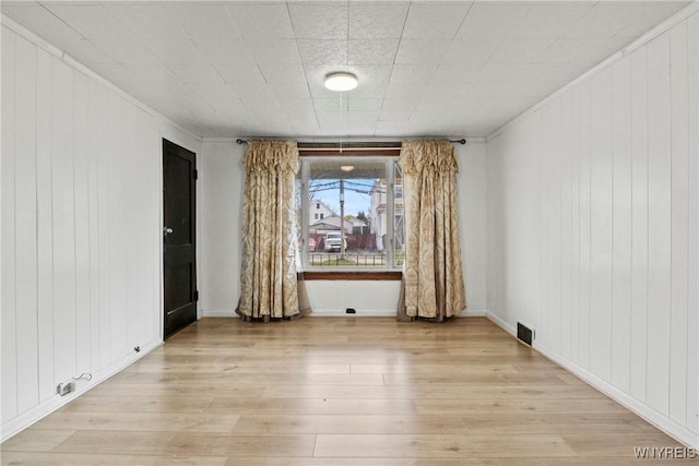 spare room with crown molding, light wood finished floors, wooden walls, and visible vents