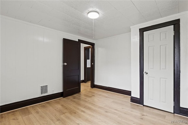 empty room featuring visible vents, baseboards, crown molding, and light wood-type flooring