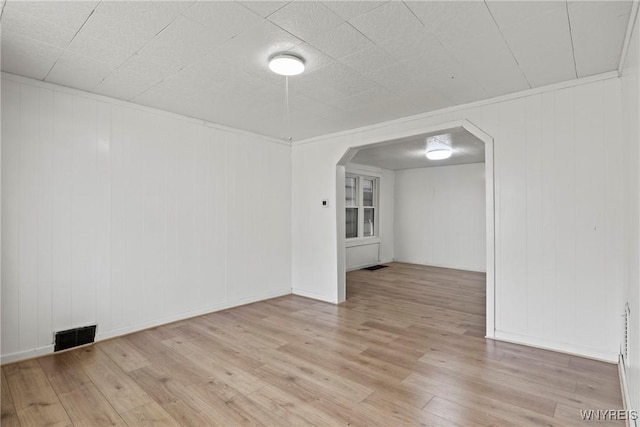 spare room with arched walkways, wood finished floors, and visible vents