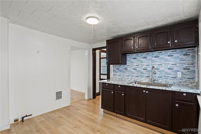kitchen with visible vents, decorative backsplash, dark brown cabinetry, a sink, and light wood-style flooring