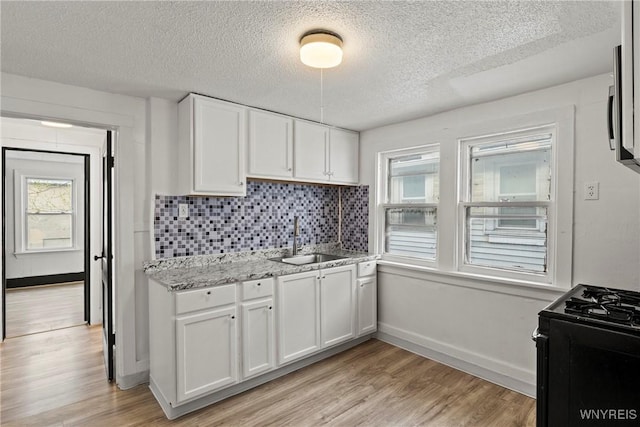 kitchen featuring black range with gas cooktop, backsplash, a textured ceiling, a sink, and white cabinets