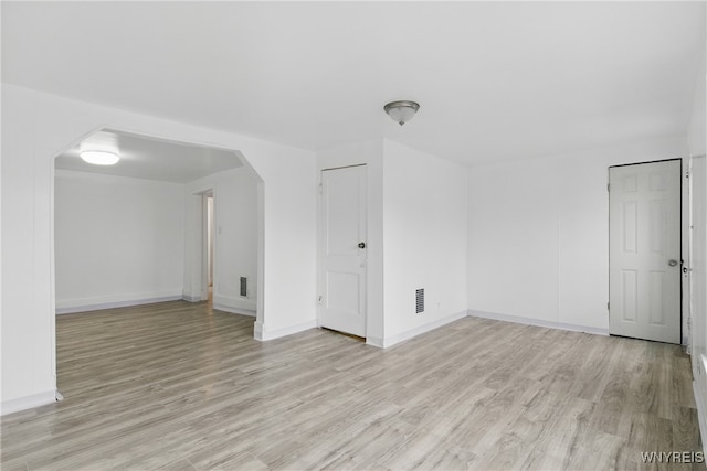 unfurnished room featuring arched walkways, baseboards, light wood-style flooring, and visible vents