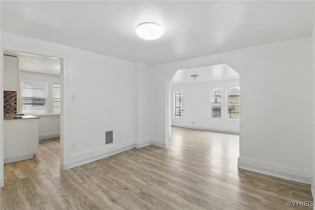 unfurnished room with plenty of natural light, arched walkways, and light wood-style flooring