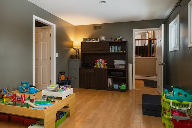 game room featuring a baseboard heating unit, light wood-type flooring, and visible vents