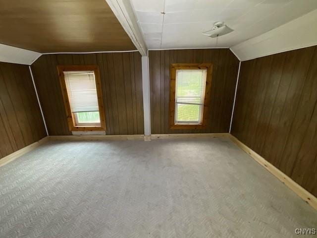 bonus room featuring wooden walls, baseboards, light colored carpet, and lofted ceiling
