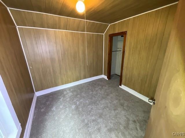 unfurnished bedroom with wood ceiling, carpet floors, baseboards, lofted ceiling, and wooden walls