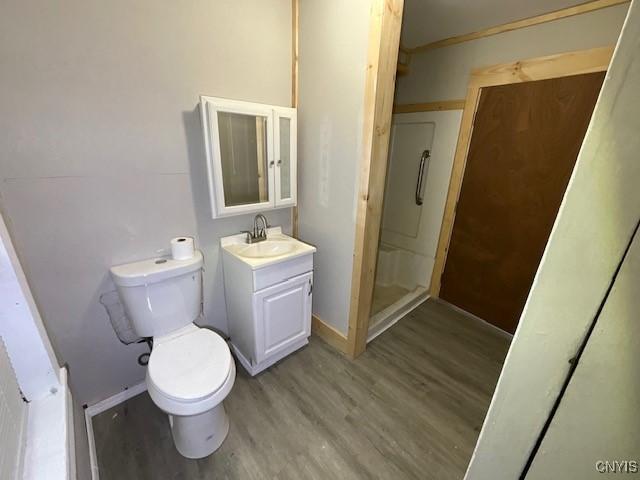 full bathroom with a stall shower, wood finished floors, vanity, baseboards, and toilet