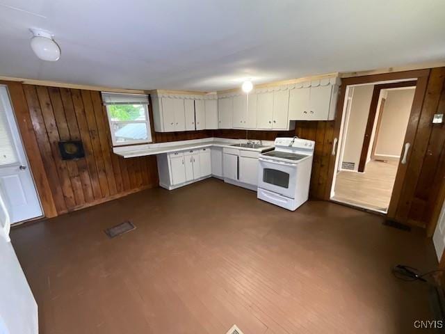kitchen featuring a sink, wood walls, electric range, and white cabinets