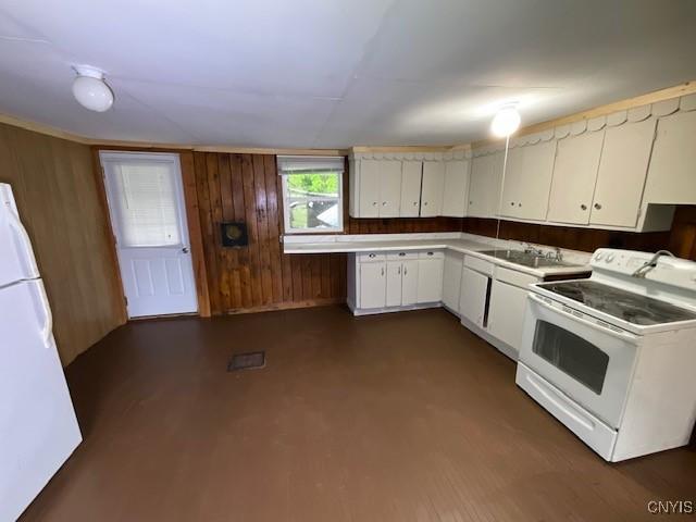 kitchen with white appliances, white cabinetry, a sink, and wooden walls