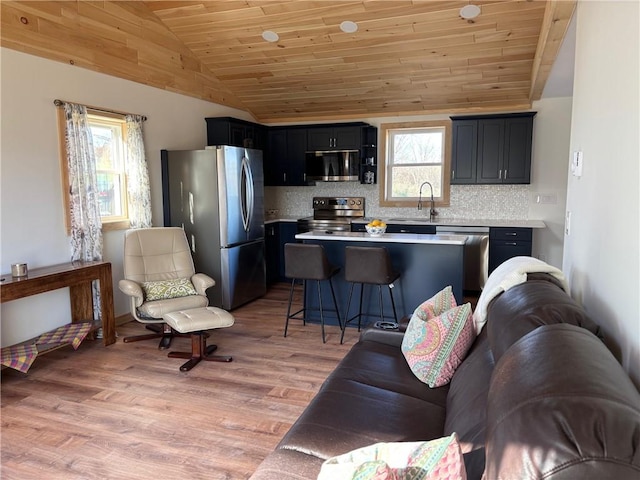 kitchen with a breakfast bar, light countertops, stainless steel appliances, tasteful backsplash, and vaulted ceiling