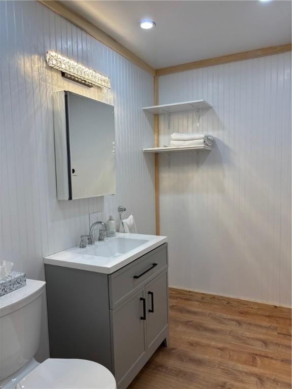 bathroom with wooden walls, toilet, wood finished floors, and vanity