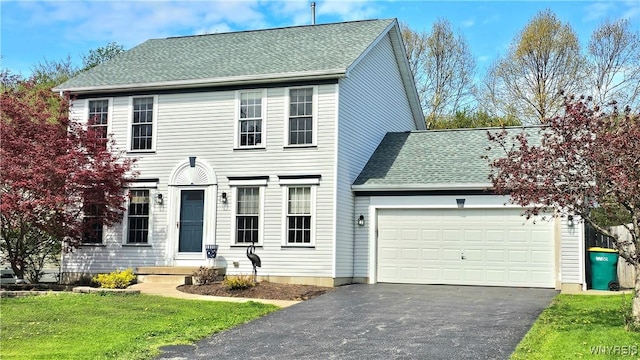 colonial-style house featuring a front yard, a garage, roof with shingles, and aphalt driveway
