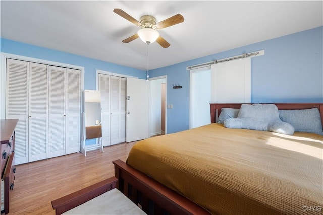 bedroom featuring two closets, a ceiling fan, a barn door, and wood finished floors