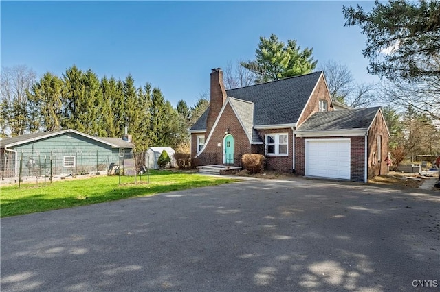 view of front facade featuring an attached garage, brick siding, aphalt driveway, a front yard, and a chimney