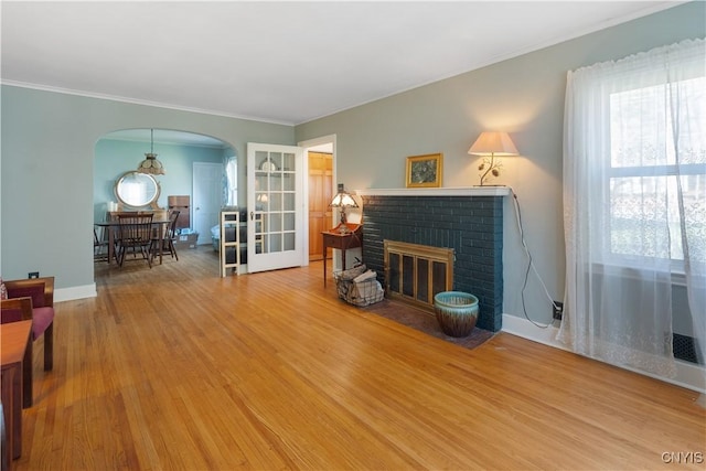 living room featuring a brick fireplace, arched walkways, ornamental molding, and wood finished floors