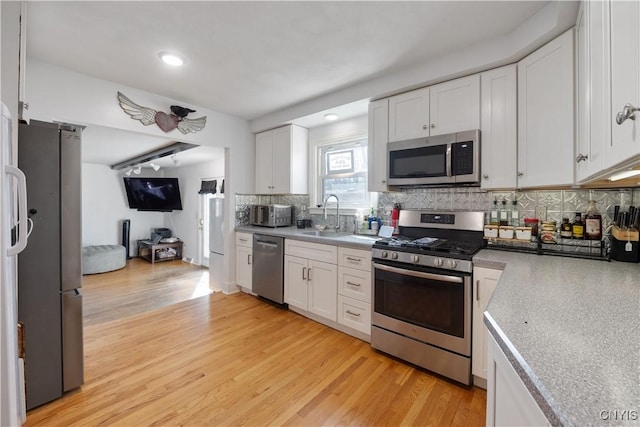 kitchen featuring a sink, light wood-style floors, stainless steel appliances, white cabinetry, and decorative backsplash