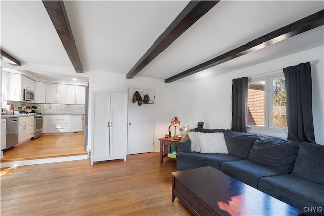 living area with beamed ceiling and light wood-style flooring