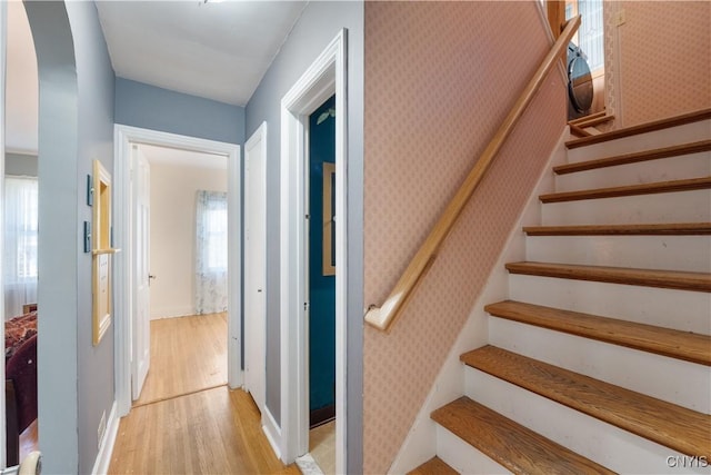 stairs featuring baseboards, arched walkways, wallpapered walls, and wood finished floors