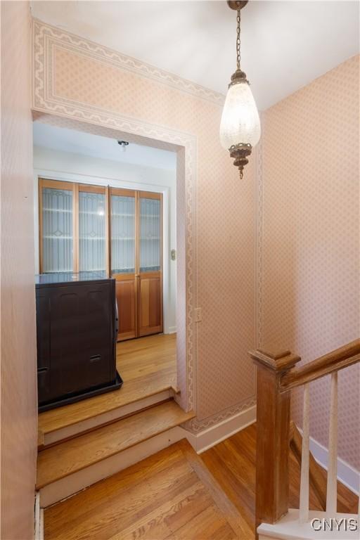 staircase with baseboards, wood finished floors, and wallpapered walls