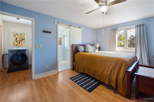 bedroom with washer / dryer, wood finished floors, baseboards, ceiling fan, and a barn door