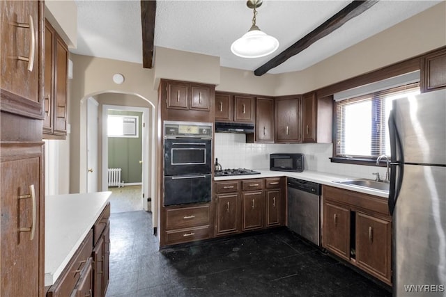 kitchen featuring a sink, arched walkways, radiator heating unit, stainless steel appliances, and a healthy amount of sunlight
