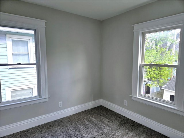 spare room featuring baseboards, a healthy amount of sunlight, and dark carpet