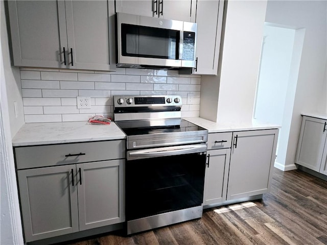 kitchen featuring appliances with stainless steel finishes, gray cabinets, decorative backsplash, and dark wood-style floors