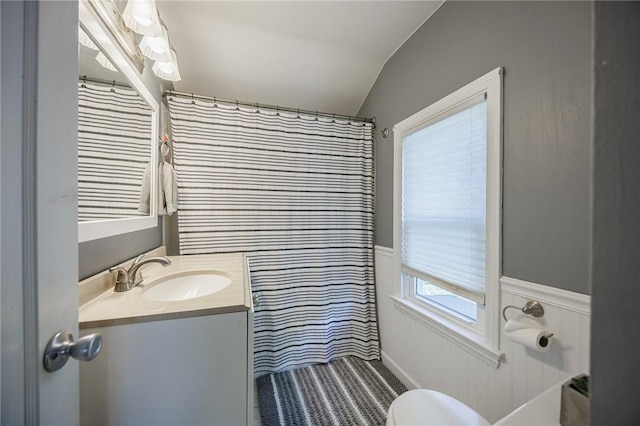 bathroom featuring vanity, lofted ceiling, toilet, and a wainscoted wall