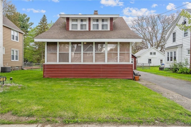 bungalow-style home with a chimney, a front yard, a sunroom, fence, and cooling unit