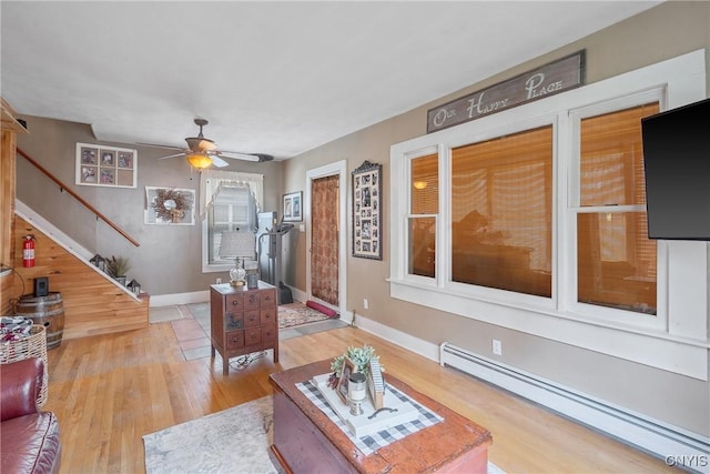 living room with ceiling fan, wood finished floors, baseboards, a baseboard radiator, and stairs