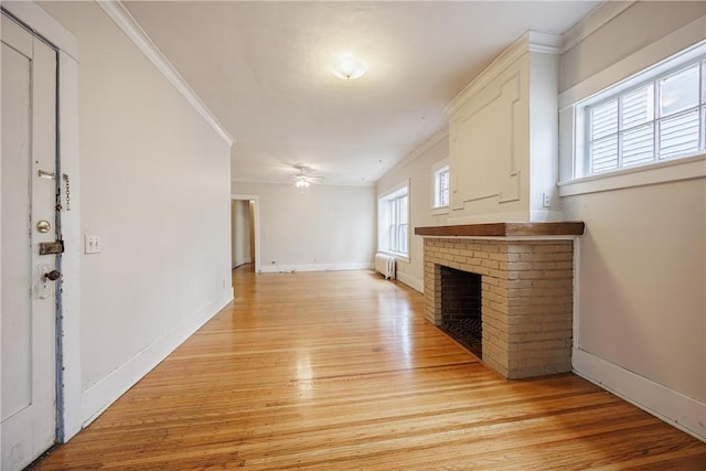 unfurnished living room featuring radiator, ornamental molding, a brick fireplace, and light wood-type flooring