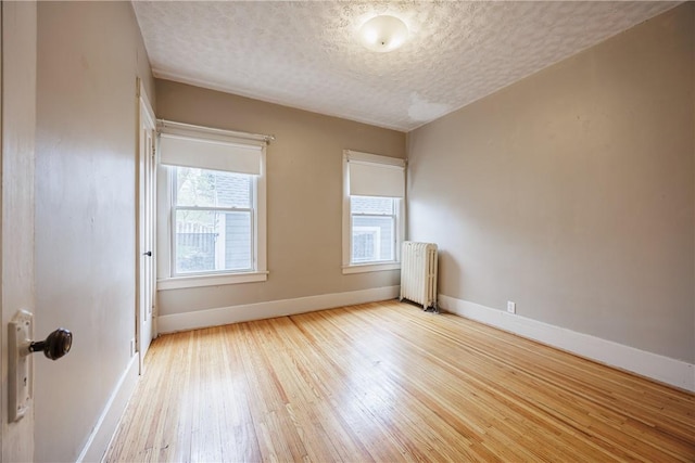 unfurnished room featuring baseboards, a textured ceiling, radiator heating unit, and wood finished floors