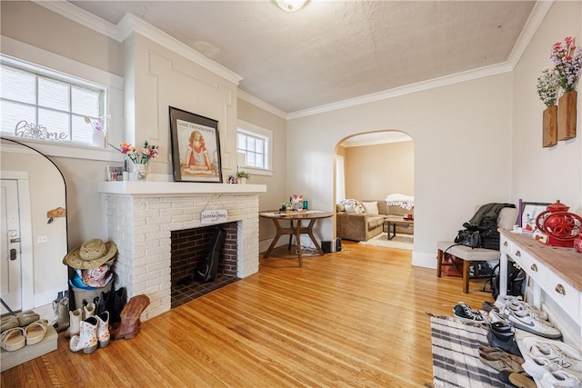 living room featuring crown molding, a fireplace, light wood-style floors, baseboards, and arched walkways