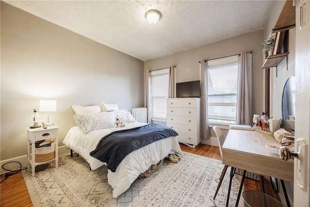 bedroom with baseboards, a textured ceiling, radiator heating unit, and light wood-style flooring