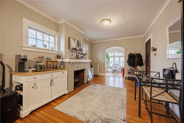 interior space featuring arched walkways, ornamental molding, radiator heating unit, and light wood finished floors