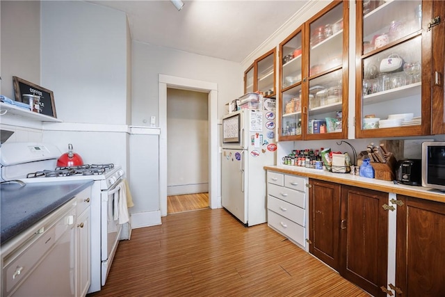 kitchen featuring light countertops, wood finished floors, white appliances, and glass insert cabinets