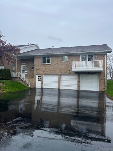 view of front of property featuring an attached garage, brick siding, a balcony, and driveway