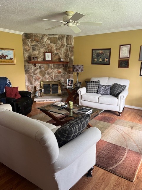 living room featuring ceiling fan, a textured ceiling, ornamental molding, and wood finished floors