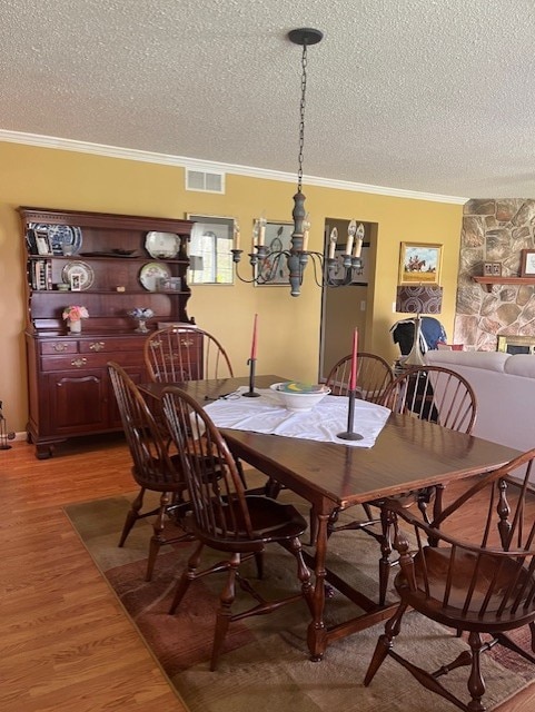 dining space with crown molding, a textured ceiling, visible vents, and light wood-style flooring