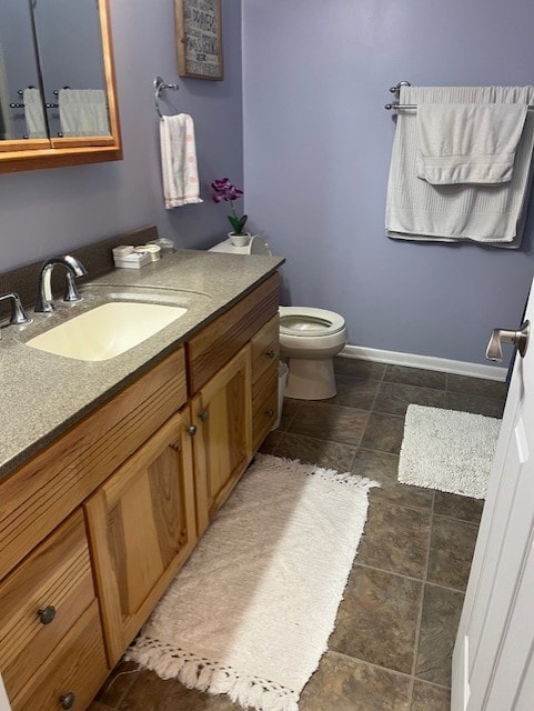 bathroom with vanity, baseboards, toilet, and stone finish flooring