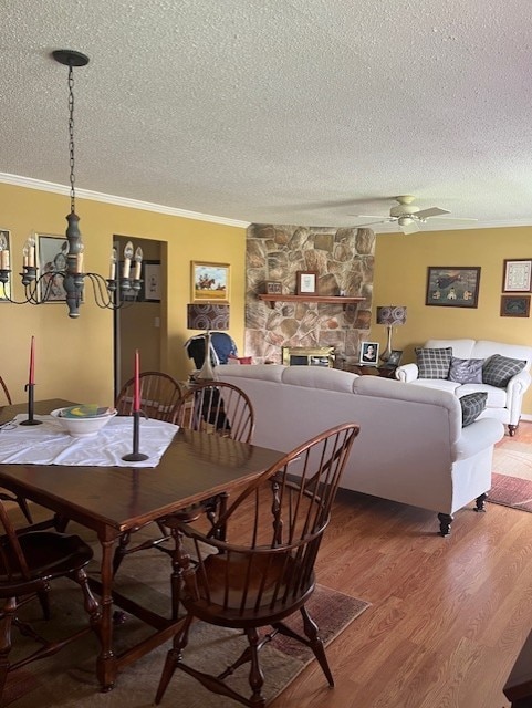 dining area featuring a stone fireplace, a textured ceiling, ornamental molding, and light wood finished floors