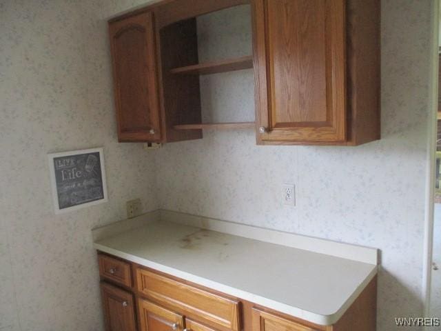 kitchen featuring light countertops, brown cabinets, wallpapered walls, and open shelves