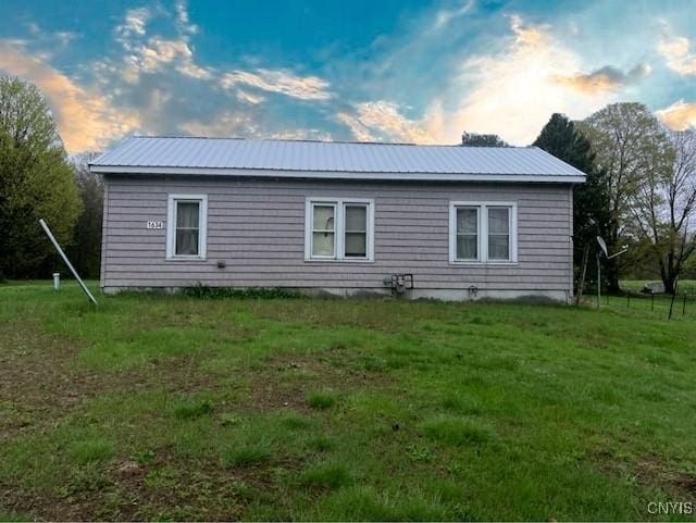 back of property at dusk with a lawn and metal roof