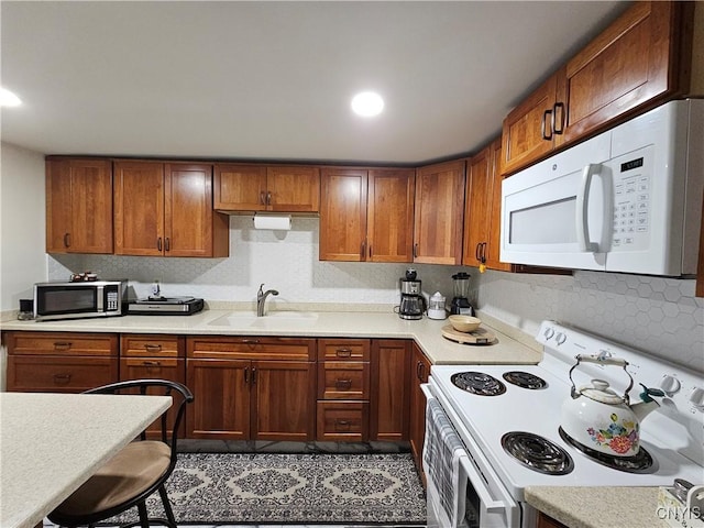 kitchen featuring brown cabinetry, a sink, white appliances, and light countertops