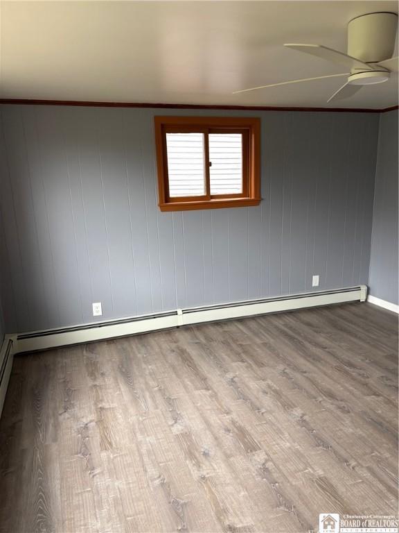 empty room featuring baseboards, a baseboard radiator, a ceiling fan, and wood finished floors