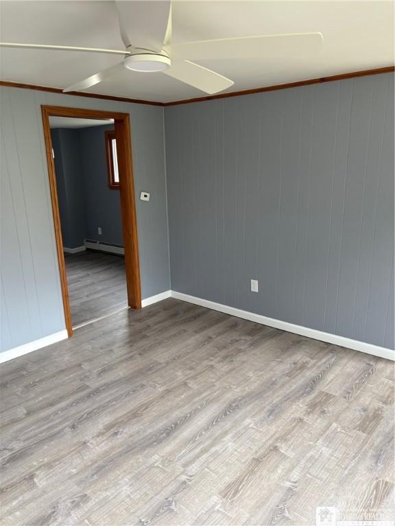 unfurnished room with ceiling fan, baseboards, wood finished floors, a baseboard heating unit, and ornamental molding