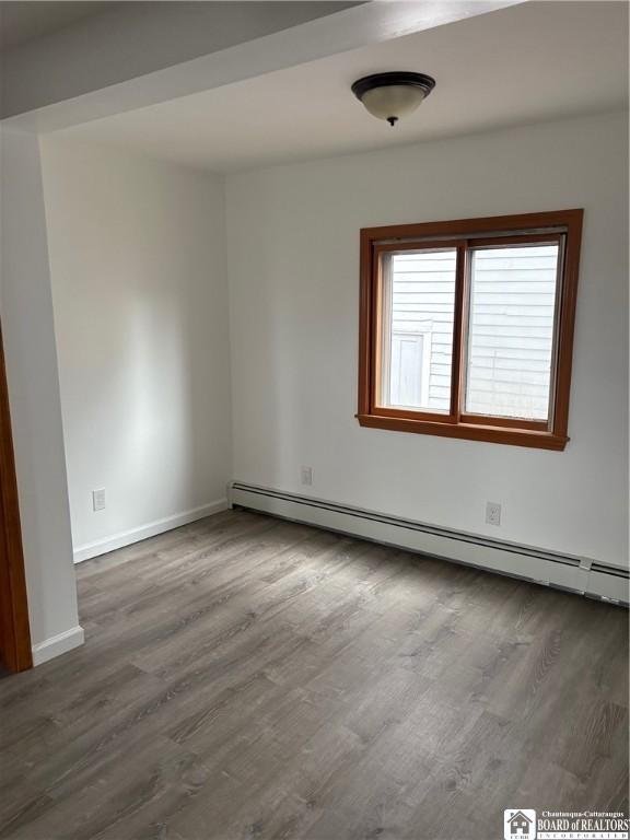 unfurnished room featuring baseboards, a baseboard radiator, and wood finished floors