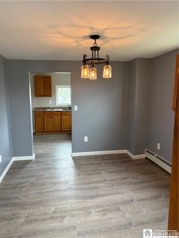 unfurnished dining area with baseboards, baseboard heating, and wood finished floors