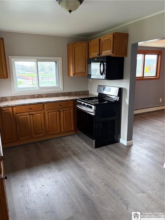 kitchen with gas stove, brown cabinets, a baseboard heating unit, and black microwave