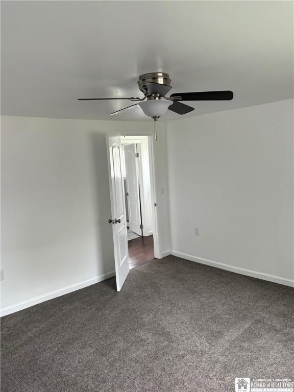 empty room featuring a ceiling fan, baseboards, and dark carpet